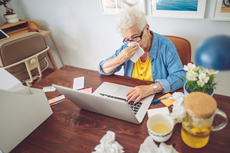 Senior woman at home on computer surrounded by used tissues.