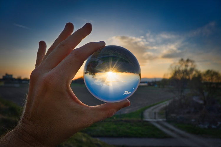 A hand holding a crystal ball looking into horizon at sunset.