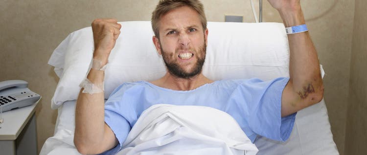 young angry patient man at hospital room lying in bed pressing nurse call button feeling nervous and upset in some kind of emergency health care and medical attention concept