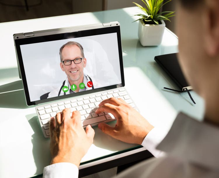 Businessman's hand videoconferencing with happy doctor on laptop