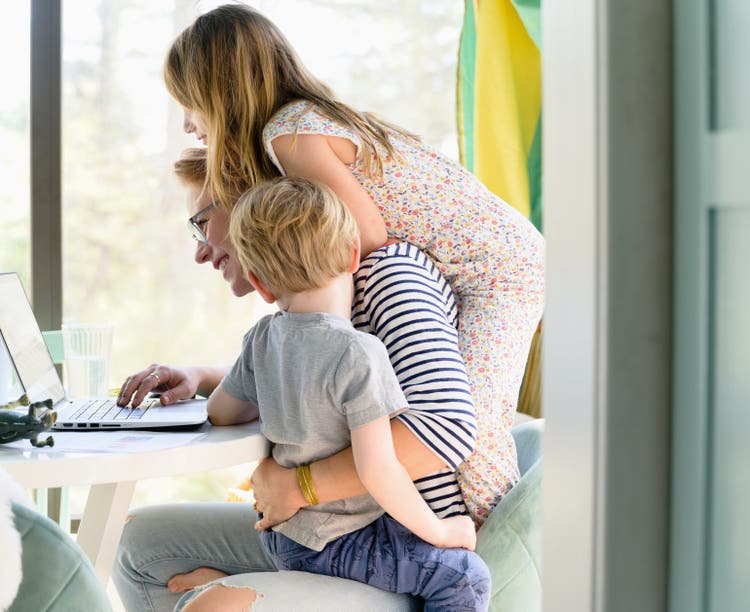 Children (4-5, 6-7) climbing on their mother while she works from home