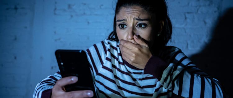 Frightened teenager or young woman using smart mobile cell phone as internet cyberbullying by message stalked abused victim.