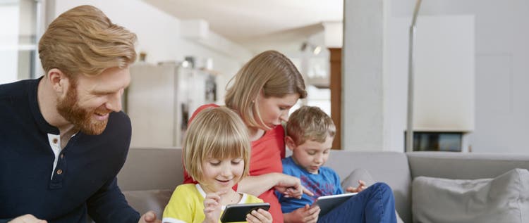 Family of four using mobile devices on couch
