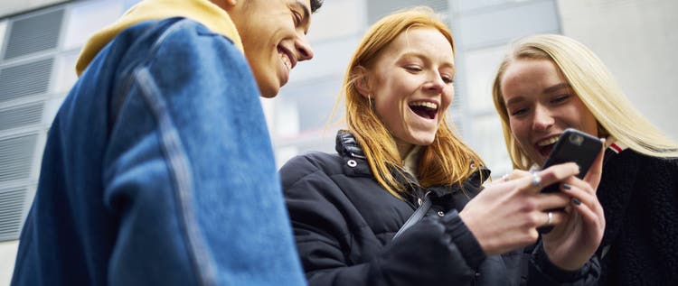 Three teens laughing and joking while looking at their phone