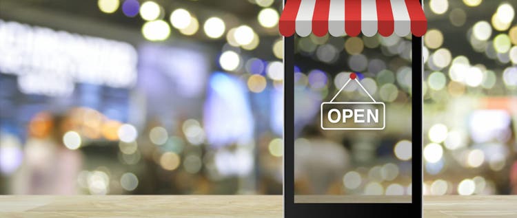 Modern smart mobile phone with on line shopping store graphic and open sign on wooden table over blur light and shadow of mall