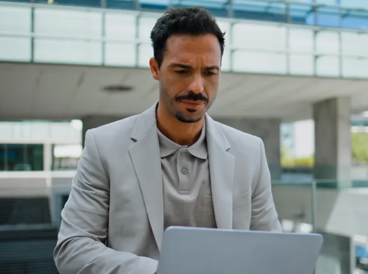 Businessman in a grey suit using a laptop outside a modern glass office building