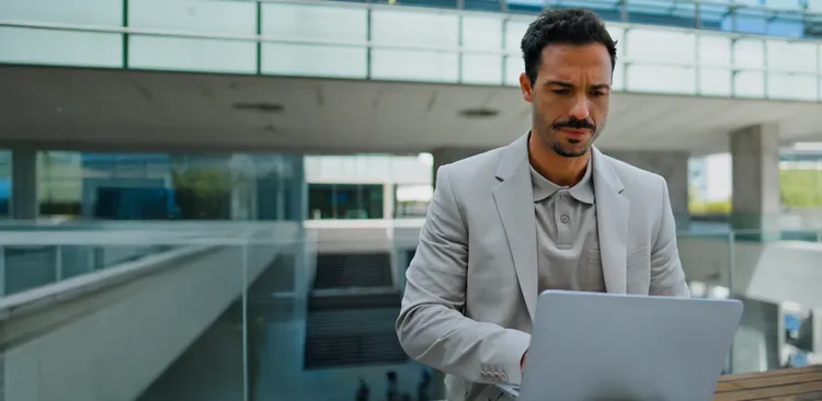 Businessman in a grey suit using a laptop outside a modern glass office building